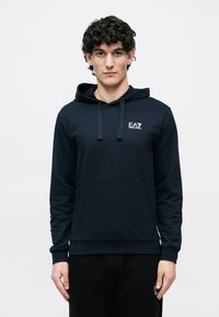 Tengerészkék kapucnis pulóver puha anyagból, elöl zsebel, húzózsinóros kapucnival és kicsi fehér logóval a mellrészen.