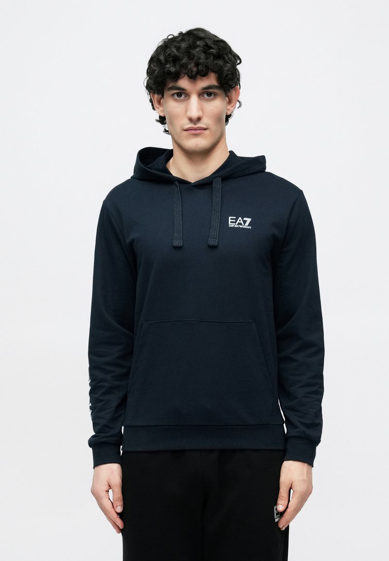 Tengerészkék kapucnis pulóver puha anyagból, elöl zsebel, húzózsinóros kapucnival és kicsi fehér logóval a mellrészen.