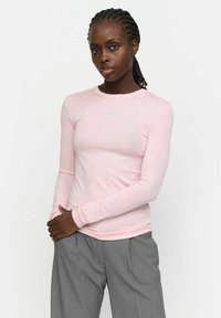 Light pink long-sleeve shirt made of soft fabric, featuring a round neckline and fitted design, paired with gray high-waisted trousers.