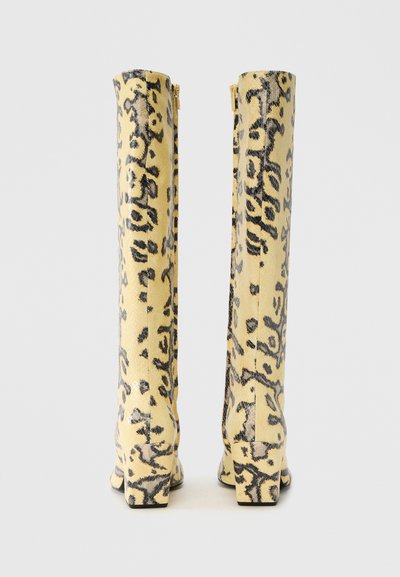 Μπότες μέχρι το γόνατο από κίτρινο δέρμα με μαύρο ζώο τύπωμα, με ελαφριά τακούνι και φερμουάρ στο πίσω μέρος.