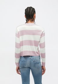 Pull rayé en rose pâle et blanc, confectionné en tissu tricoté léger. Modèle court avec manches longues et ourlet côtelé. Porté avec un jean bleu.