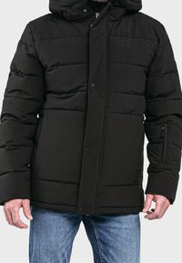 Giubbotto puffer nero con cappuccio, dotato di imbottitura trapuntata, chiusura a bottoni automatici e tasca laterale con zip. Il materiale appare liscio e opaco.