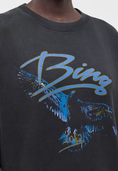 Μαύρο φούτερ με μπλε και κίτρινο κείμενο "Bing" και εικονογραφημένο μπλε πουλί με απλωμένα φτερά, με ημερομηνία "2013" κάτω από το πουλί.