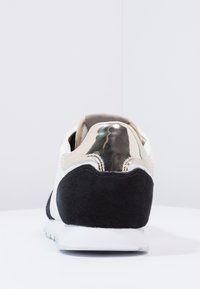 Tenisky s černým semišovým podpatkem, bílým textilním tělem a kovovými akcenty. Zaoblený tvar, polstrovaný límec, textura podrážky, minimální branding.