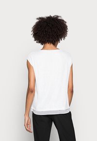 Top blanco de manga corta con un acabado texturizado, que cuenta con un escote redondeado y un dobladillo con capas. La tela tiene un brillo sutil.