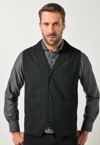 Schwarze Stoffweste mit Reverskragen, fünf Knöpfen und einer Brusttasche, kombiniert mit einem grauen Langarmhemd. Glatte Textur, maßgeschneiderte Passform.
