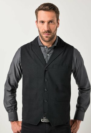Chaleco de tela negra con cuello de muesca, cinco botones y un bolsillo en el pecho, combinado con una camisa gris de manga larga. Textura suave, ajustado a medida.