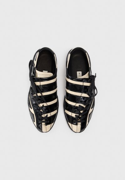 Black and cream striped sneakers with a textured patent finish, featuring lace-up design and rounded toe.