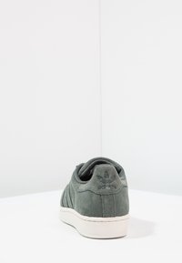 Zapatillas de ante gris con suela de goma blanca. Presenta un logo en relieve en el talón, rayas laterales texturizadas y un diseño de punta redonda.