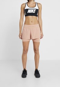 Czarno-biały sportowy biustonosz Nike z szarymi akcentami, zestawiony z jasnoróżowymi szortami sportowymi o warstwowej konstrukcji i perforacjach. Czarne buty sportowe.