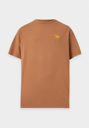 Brun kortærmet t-shirt med rund hals og lille gul løvegrafik på venstre bryst mod en lys baggrund.