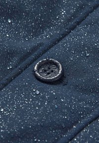 Vandafvisende mørk navy stof med synlige vanddråber; har en sort knap med fire huller, struktureret overflade og fine sting.