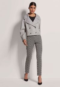 Graue, doppelt knöpfbare, verkürzte Jacke mit großen Knöpfen, kombiniert mit schwarz-weiß gemusterten, schmal geschnittenen Hosen und schwarzen High Heels.