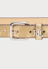 Gullfarget faux skinnbelte med en sølvfarget metallspenne som har et gravert "RL"-logo. Beltet har synlige sømmer og justeringshull.