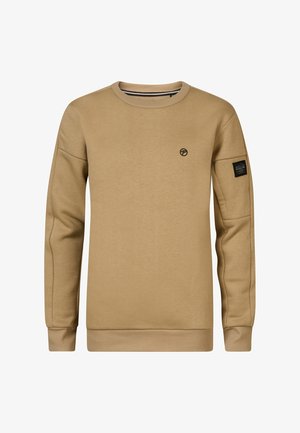 Beżowa bluza z długimi rękawami i okrągłym dekoltem, zestawiona z niebieskimi dżinsami. Obuwie to czarno-białe sneakersy w wzory.