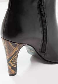 Černá kožená kotníková bota se bočním zipem, s podpatkem s hnědým a černým hadím vzorem. Hladký povrch, design se špičatou špičkou.