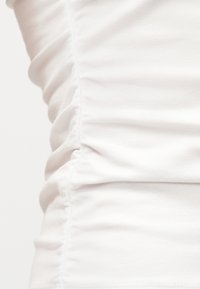 Close-up van witte stof met geplooide en gerimpelde details langs een zijnaden, met zichtbare textuur en plooien.