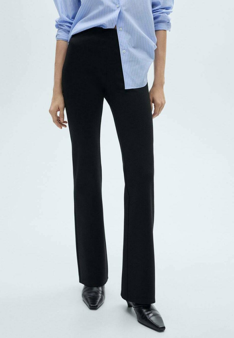 Black flared trousers made of stretchy fabric, featuring a high waistband and a slight split at the hem, paired with a light blue striped shirt.