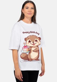 Wit T-shirt met een cartoonotter die een taart vasthoudt met roze glazuur en kersen, boven de tekst staat "Gefeliciteerd." Korte mouwen, losse pasvorm.