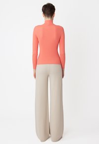 Langärmliger, gerippter Rollkragenpullover in Koralle, kombiniert mit beigen, weit geschnittenen Hosen. Glatte Textur, körpernahe Passform, mit kontrastierender Farbpalette.