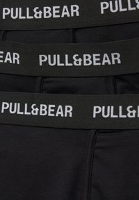 Crni bokserice s širokim elastičnim pojasom na kojem je bijelim slovima ispisano "PULL&BEAR". Glatka tkanina s uskim krojem.