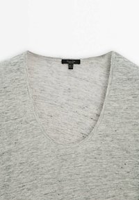 T-shirt gris clair chiné avec un col en V et une étiquette noire à l’intérieur du col indiquant le nom de la marque.