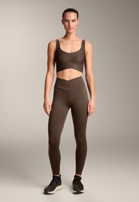 Barna sportos cropped top és magas derekú leggings sima, rugalmas anyagból. V-alakú részlet található a deréknál.