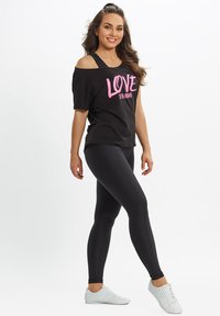 Black off-the-shoulder t-shirt with pink text “LOVE is the ANSWER,” paired with black leggings and white athletic shoes. Smooth fabric, casual fit.