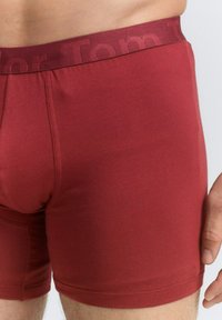 Rote Baumwoll-Boxershorts mit einer figurschmeichelnden Passform, ausgestattet mit einem weichen elastischen Bund. Der Stoff wirkt glatt mit einem leichten Glanz.