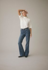 Biała koszulka z krótkim rękawem i golfem w połączeniu z niebieskimi rozszerzanymi jeansami. Strój uzupełnia czarny pasek oraz czarne buty z ostrym noskiem.