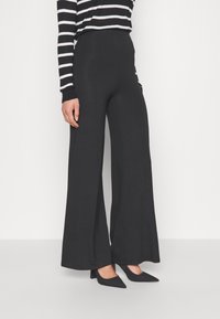 Szerokie czarne spodnie wykonane z miękkiego materiału, z wysokim stanem i gładką fakturą. Połączone z czarno-białą, w paski koszulą z długim rękawem.