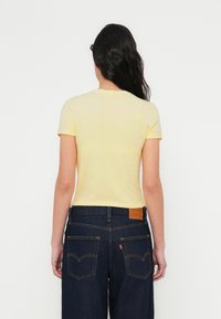 Keltainen puuvillainen t-paita, jossa klassinen leikkaus ja lyhyet hihat, yhdistetty tummansinisiin farkkuihin, joissa on nahkainen logoplässi ja takataskut.