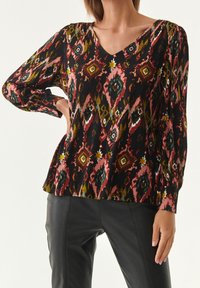 Blouse à manches longues en tissu multicolore à motifs, arborant un décolleté en V, avec une coupe décontractée et des détails texturés.