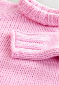Pulover roz tricotat cu guler cu nervuri. Materialul este lână moale, groasă, cu modele de tricot verticale și orizontale.