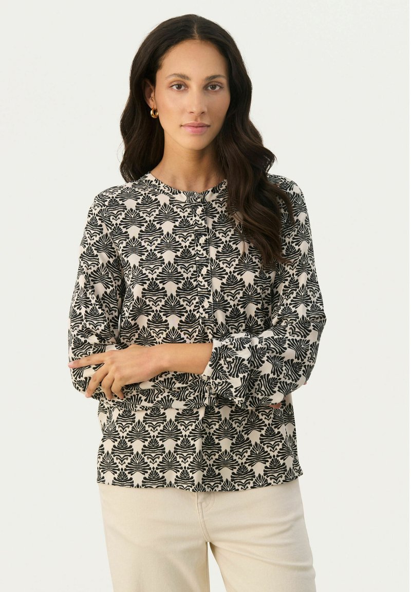 Zwart-witte blouse met een patroon, lange mouwen, ronde halslijn en knoopdetails. De stof lijkt licht en soepel.