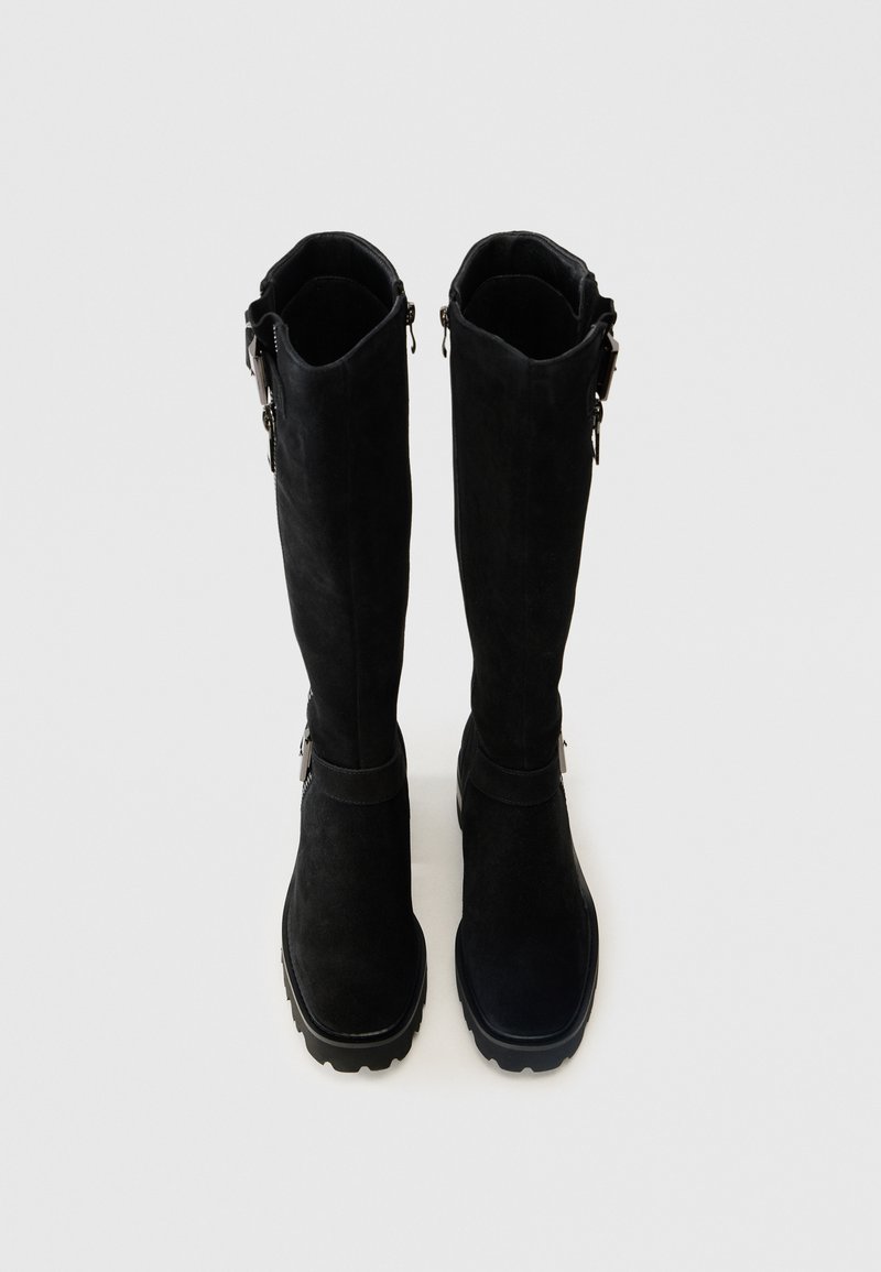 Botas negras hasta la rodilla de ante, con una textura suave, cierre de cremallera en el costado y una suela de goma gruesa para mayor tracción.