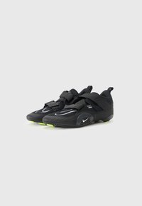 Chaussures de sport noires avec tige en mesh, bandes noires contrastantes, accents réfléchissants et semelle extérieure verte lumineuse. Design léger pour plus de flexibilité.