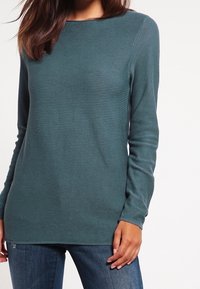 Turquoise trui met lange mouwen, geribbelde textuur en een ronde halslijn, gecombineerd met een blauwe spijkerbroek. Rechte zoom en een slim-fit ontwerp.