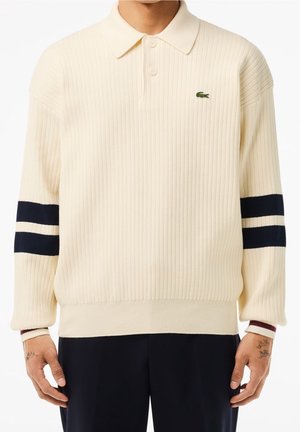 Pull polo crème côtelé à manches longues avec deux bandes bleu marine sur chaque manche et un petit logo crocodile vert sur la poitrine.