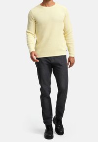 Pull à rayures jaune clair, à manches longues et col rond ; associé à un jean foncé et des chaussures noires à lacets. Design simple et texturé.