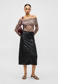 Sieviete valkā plecus atsegšanu rūtainu topu, melnu midi ādas svārku, melnas papēžu sandales un nes tumši sarkanu plecu somu.