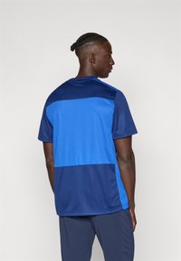 Κοντομάνικη αθλητική μπλούζα σε μπλε και ναυτικό χρώμα, με σχέδιο σε χρώματα και ελαφρύ, αναπνεύσιμο ύφασμα. Κανονική εφαρμογή με στρογγυλή λαιμόκοψη.