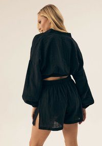 Czarny lniany zestaw dwuczęściowy, składający się z krótkiej bluzki z obszernymi rękawami oraz szortów z elastycznym pasem i bocznymi wykrojami, z efektowną teksturą.