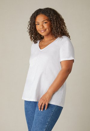 Witte korte mouw t-shirt met een v-hals, losse pasvorm en opgerolde mouwen, gemaakt van lichte stof, gedragen met blauwe jeans.