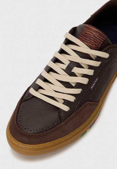 Baskets marron avec une tige en cuir et suède, des lacets crème, une semelle en gomme et un patch logo texturé près de la languette.