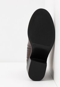 Brązowy but z gumową podeszwą, teksturowanym wierzchem i dekoracyjnym przeszyciem, z zaokrąglonym noskiem i niskim obcasem typu klockowego. Rozmiar 37.