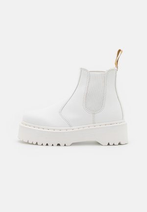 Bottine Chelsea en cuir blanc avec semelle épaisse rainurée, panneaux latéraux élastiques et languette beige au talon, présentée de profil sur fond blanc.