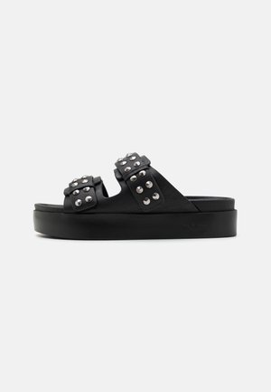 Zwarte platformsandalen met twee gespen met studs en een dikke zool op een effen achtergrond.