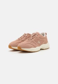 Blush pink sneaker with suede upper, lace closure, and cushioned beige sole. Features textured detailing and subtle logo on the side.
