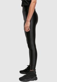 Leggings neri realizzati in un materiale lucido e elastico, con una vita alta e una vestibilità aderente. Indossati con sneaker nere testurizzate.